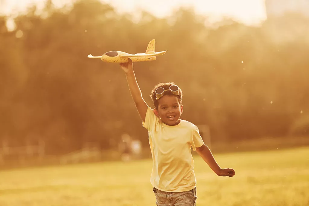 kid plying with toy airplane outside.