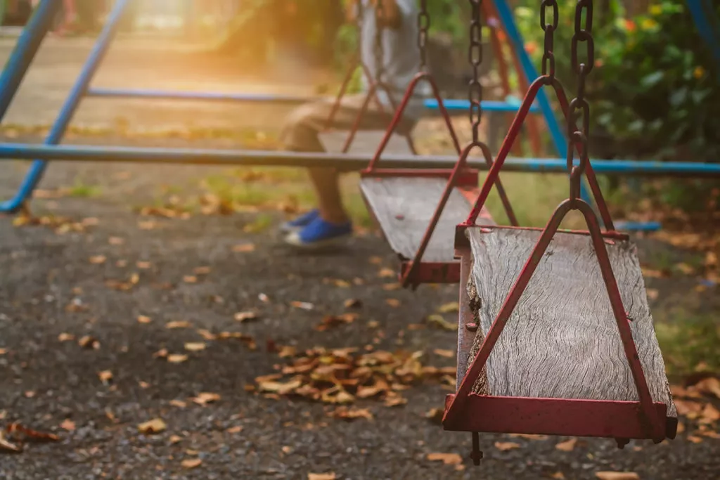 boy struggling to make friends sits alone on a swing