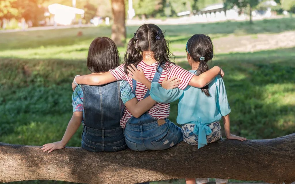 3 School Aged girls sitting outside and with their hands around each other at an After-school program at a Rockville daycare.