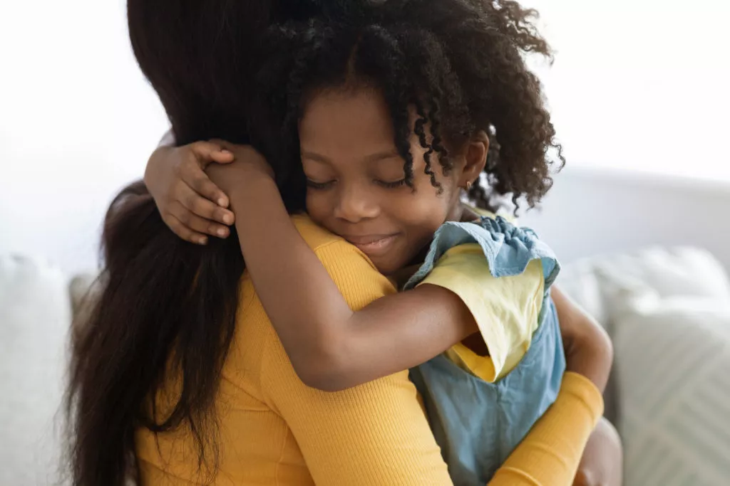 Cute Litttle African American Girl Embracing Her Mommy While Bonding Together At Home, Loving Preteen African American Female Child Hugging Mother, Enjoying Spending Time With Mom, Closeup Shot