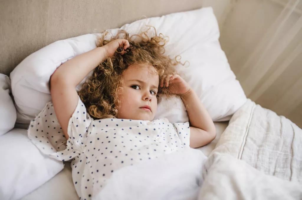 Cute charming curly-haired baby girl lying in bed on a white pillow. The concept of childhood.