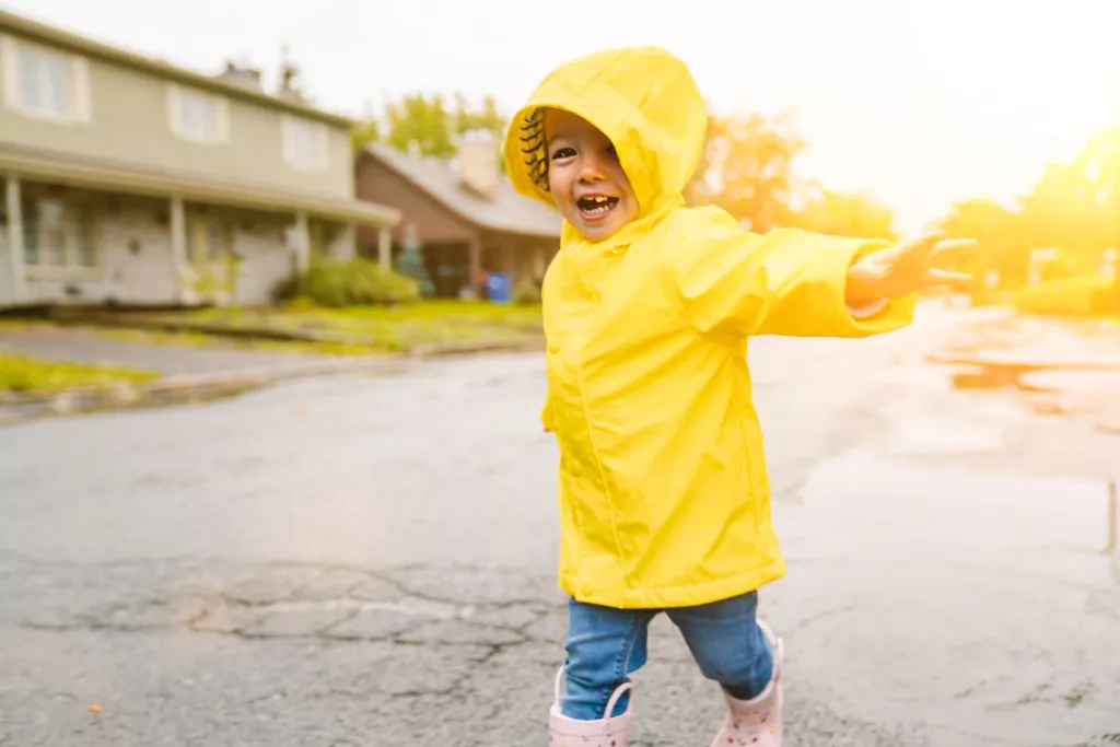 A Funny cute baby girl wearing yellow waterproof coat and boots playing in the rain