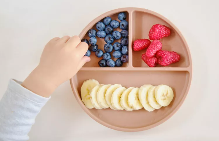 toddler hand grabbing berries as a healthy after school snack