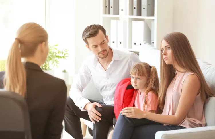 why children act out in school: couple with daughter meeting with teach discussing why children are acting out in school