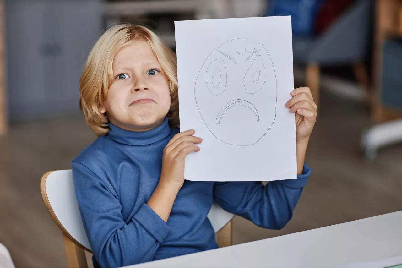child learning emotional vocabulary. Kid draws sad face and poses next to it