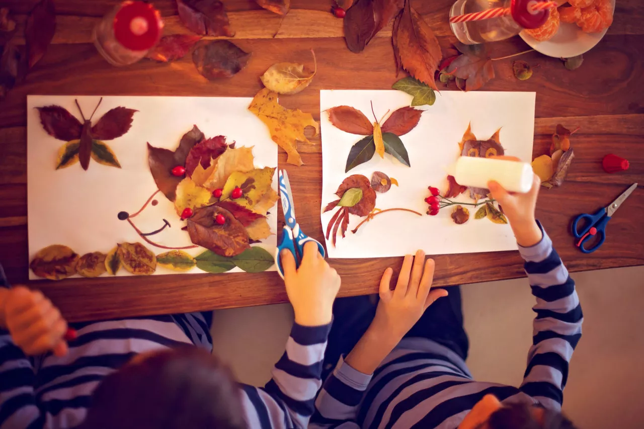 easy fall leaf crafts: Sweet child, boy, applying leaves using glue while doing arts and crafts in school, autumn time