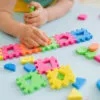 independent play in toddlers: little girl playing at a children's table with a puzzle, early education. Bright soft blocks