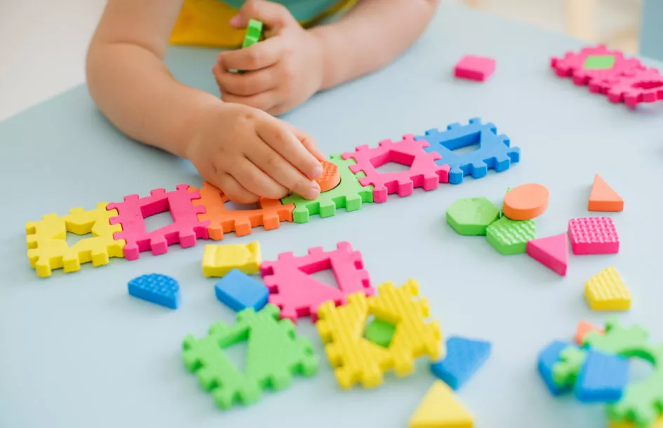 independent play in toddlers: little girl playing at a children's table with a puzzle, early education. Bright soft blocks