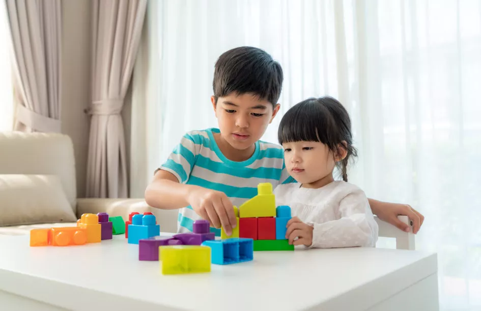 how to help siblings get along: brother and sister play with a toy block designer on the table in living room at home. Concept of bonding of sibling, friendship and learn through play activity for kid development.