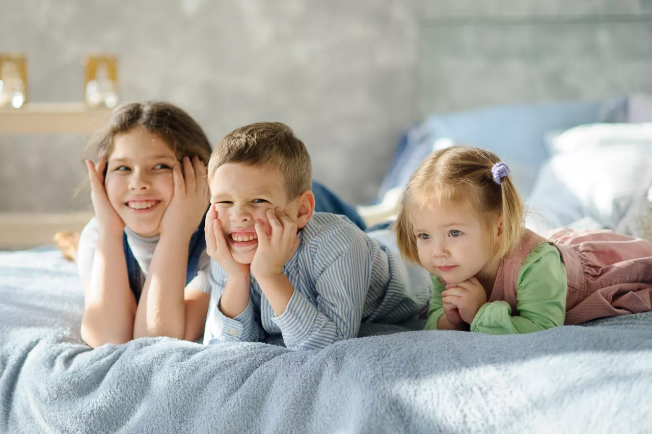 How to help siblings get along: Two sisters and a brother. Three children from the same family are lying on the bed.