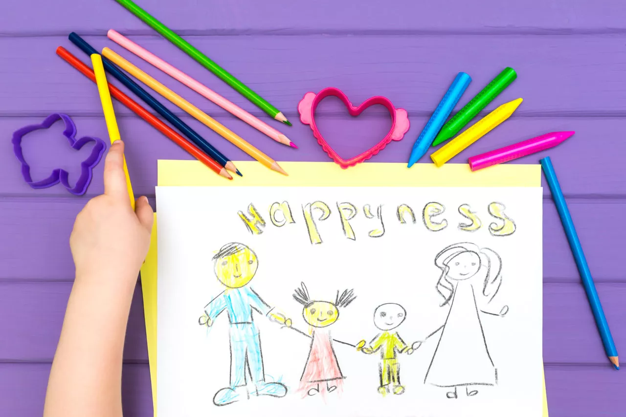 Building emotional vocabulary in preschoolers: child paints a sketch of the family with colored pencils on a white sheet of paper. The word happyness is written on the sheet