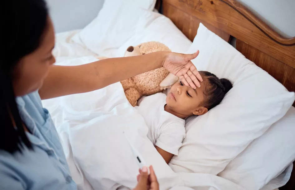 When should kids stay home from school: Thermometer, fever and mom with sick girl lying in bed, touching forehead to feel body temperature. Family, healthcare and mother with young child in bedroom