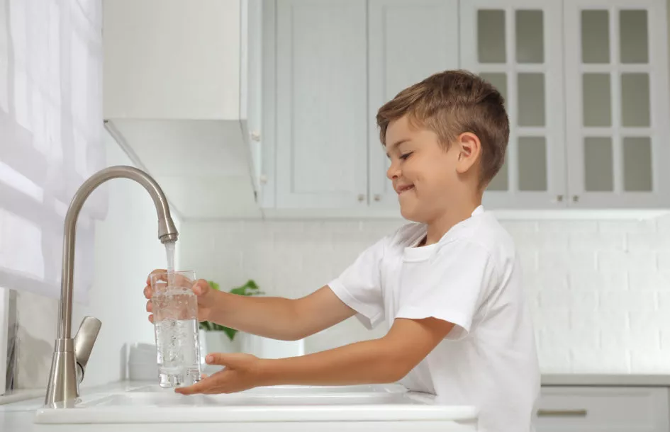 Boosting childrens immunity by staying hydrated: Boy filling glass with water from tap in kitchen