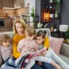 A mother and her three daughters are sitting on the couch in the living room, listening carefully to their mother reading a story, story telling activities for preschoolers