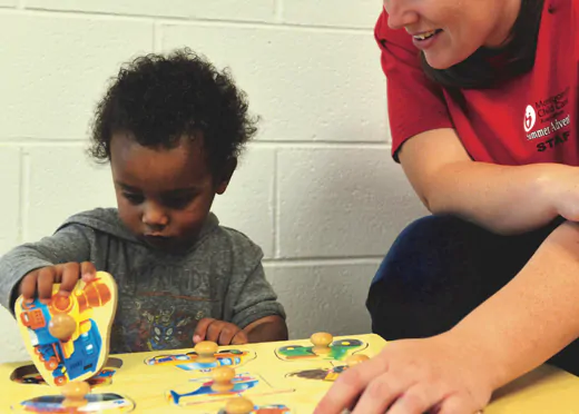 Child and educator engaged in a puzzle game at a preschool in Potomac MD, focusing on problem-solving skills.
