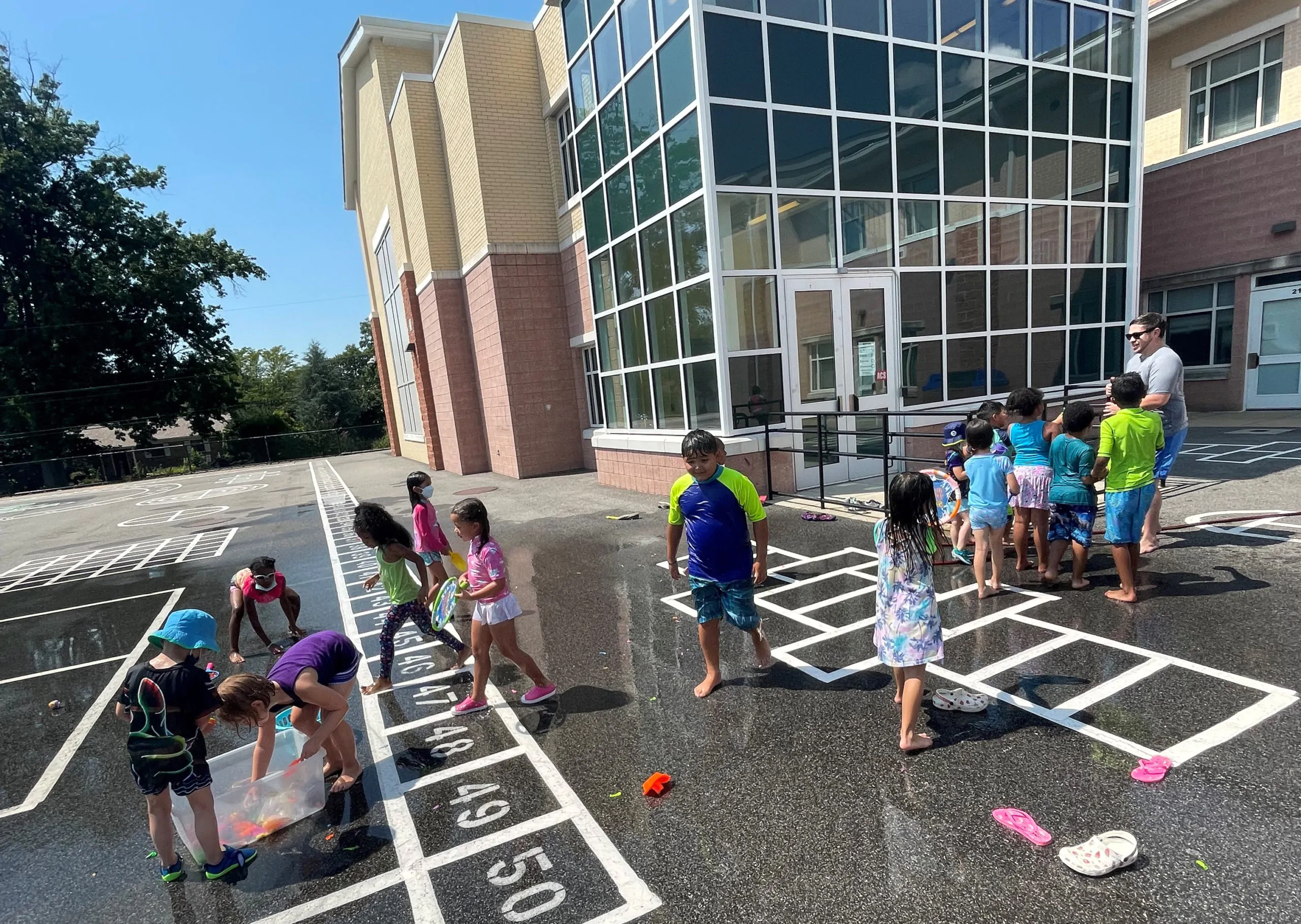 Children enjoying water play while learning numbers with hopscotch on a sunny day at Arcola Preschool.