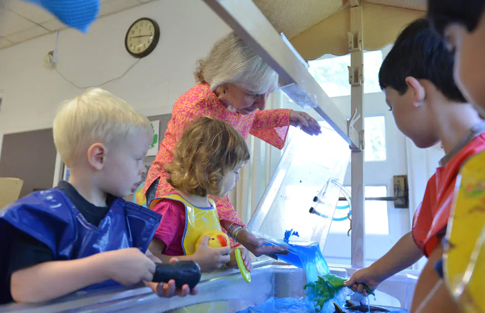 Teacher assisting children at Silver Spring Preschool water play station in Maryland.