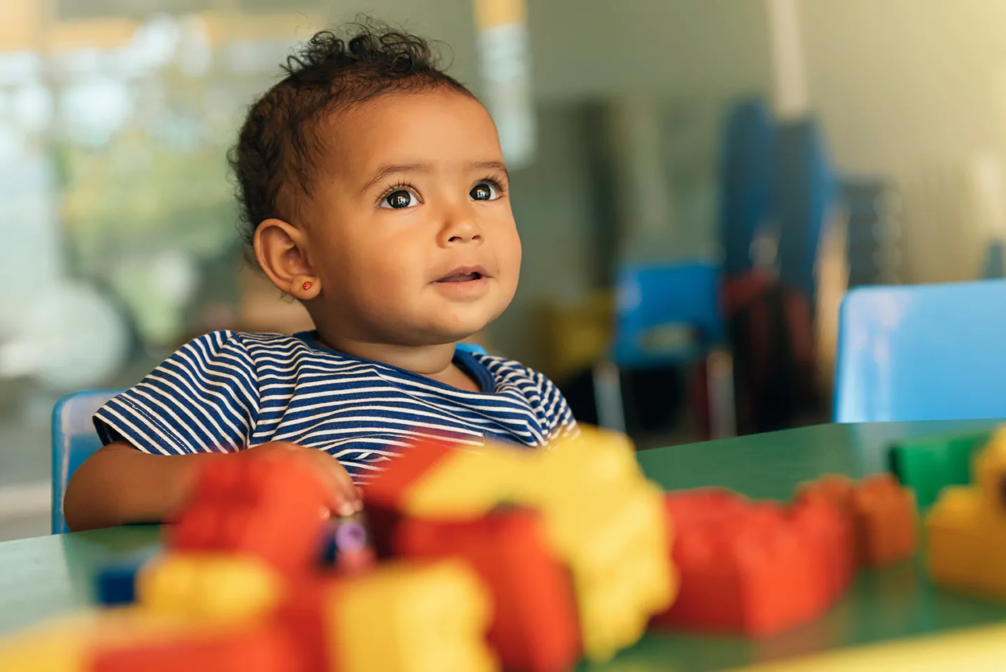 A thoughtful child at a daycare center in Rockville, MD looking at building blocks, engaging in early learning and problem-solving.