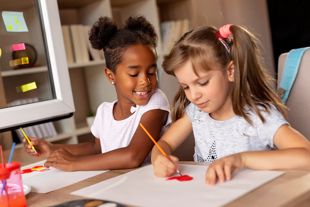Two little girls sitting at a desk, painting with water colors and having fun
