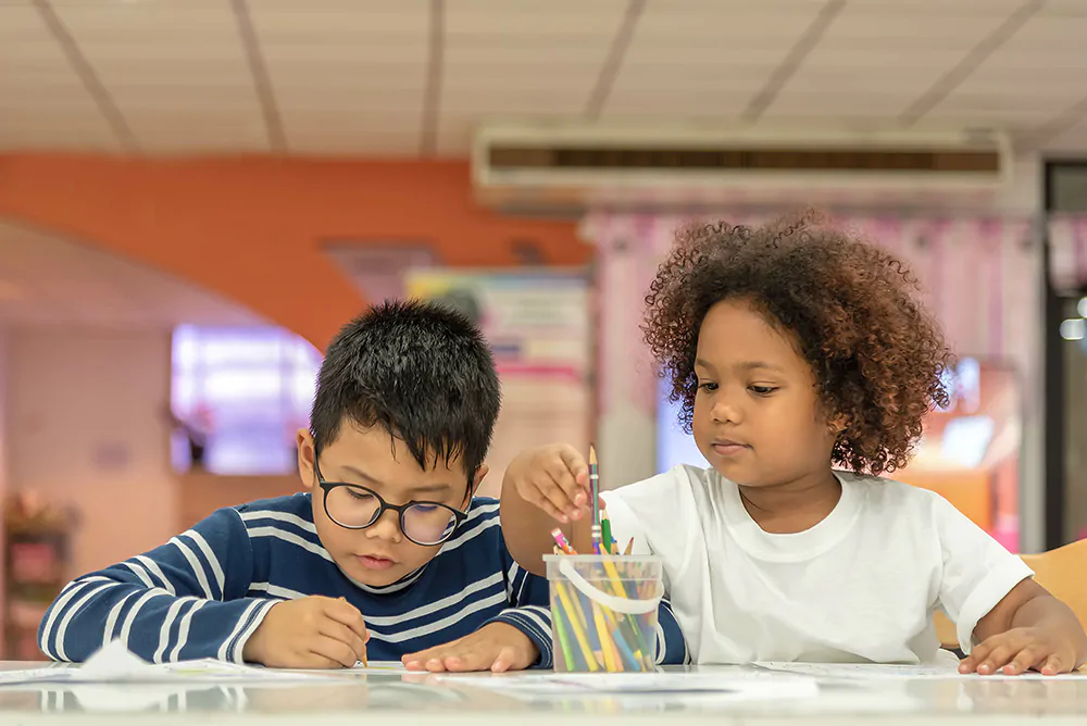 two kids sitting in a table in childcare and drawing together
