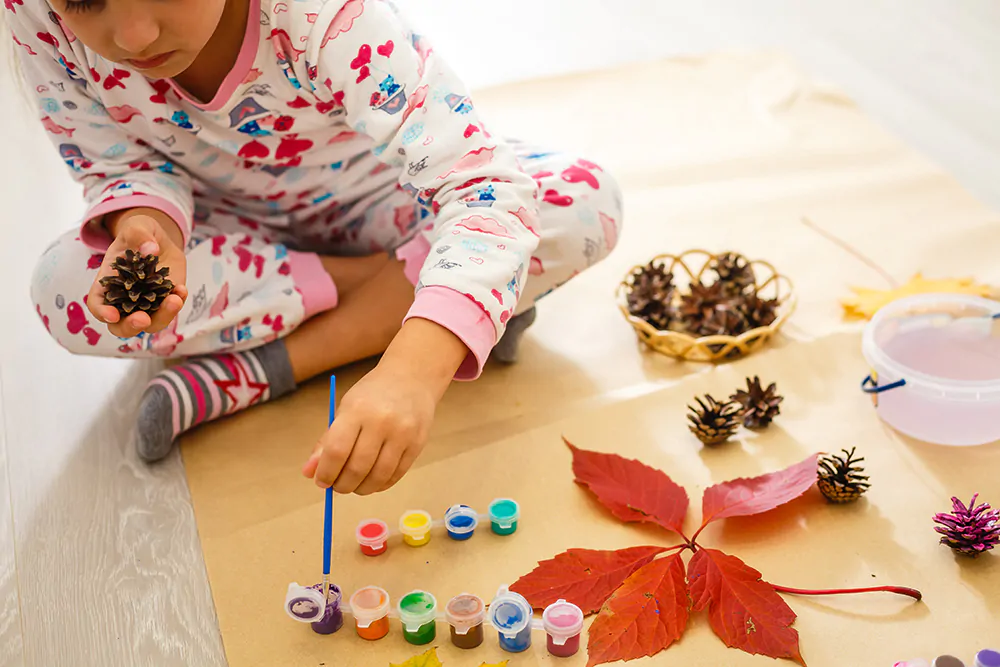 kid painting leaves and pinecones