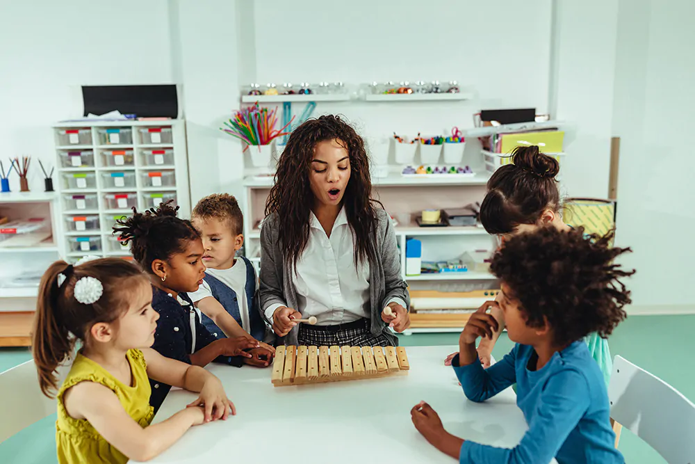 Teacher and adorable children being creative with musical toys at preschool