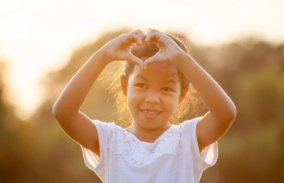 girl making heart shape with hands in the field with sunlight