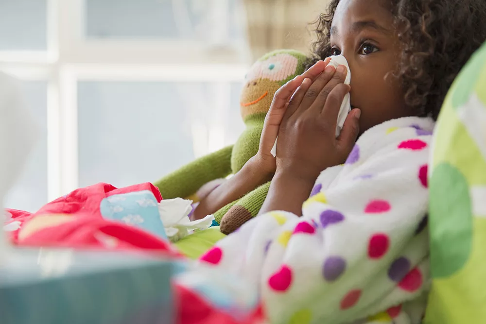Young girl blowing nose into tissue