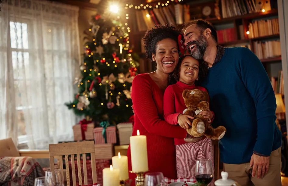 Happy family standing next to table full of ornaments on it, hugging and enjoying Christmas together.