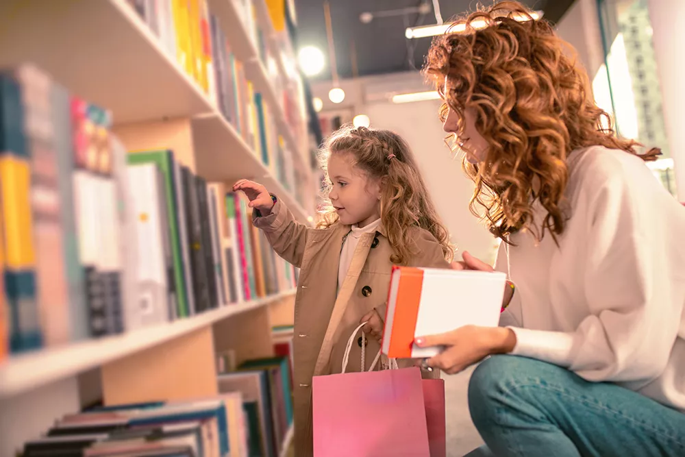 preschooler at the library looking at books with her mom or teacher