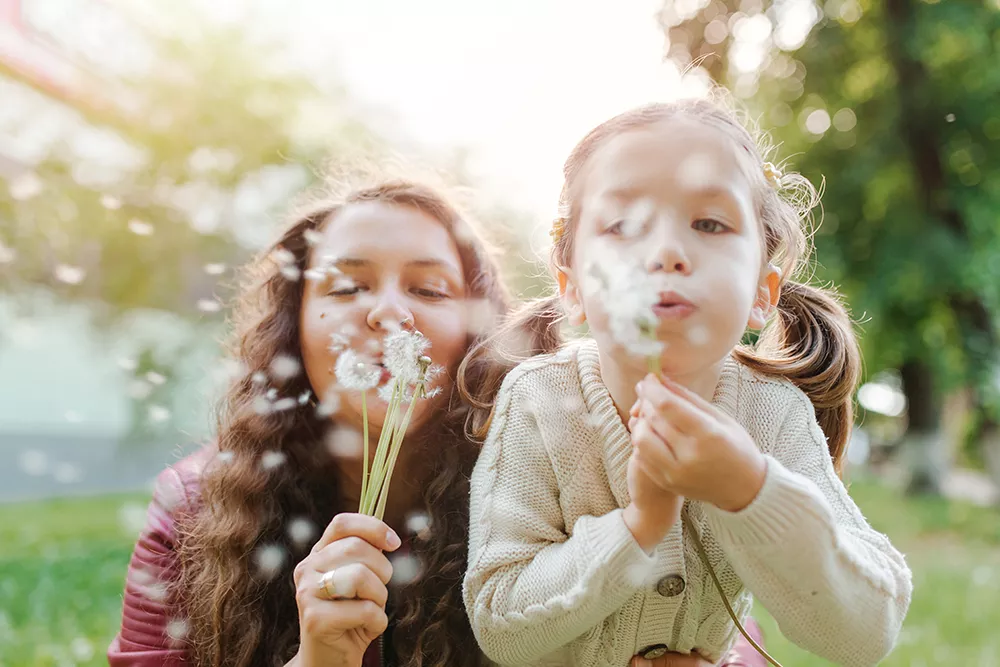 woman and child blowing on flowers