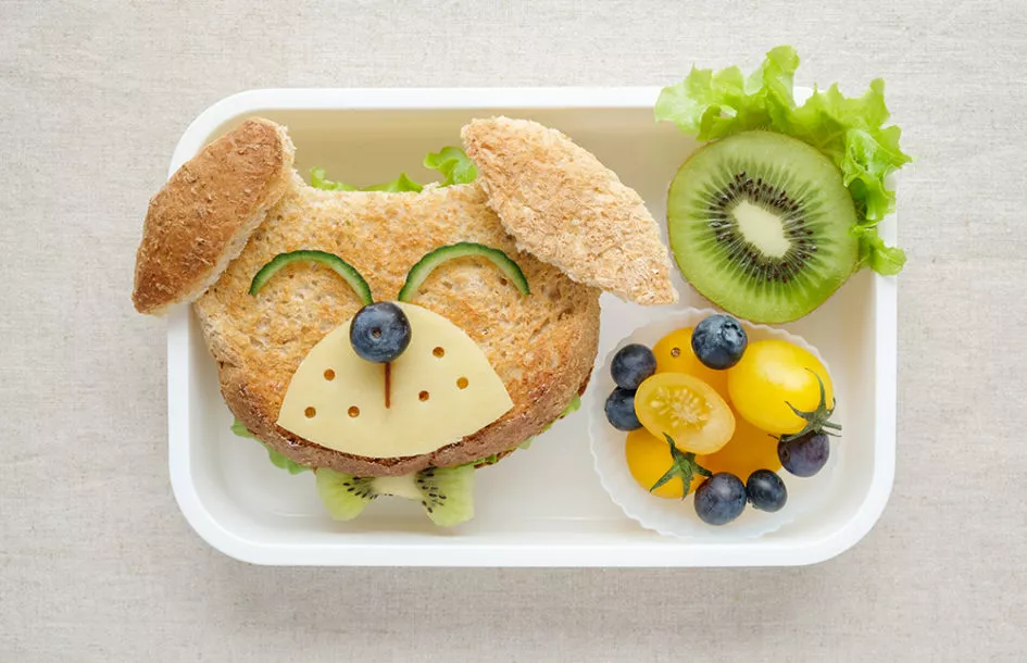 Kids lunchbox filled with cute lunch ideas including fruits and sandwich in a form of a dog with a face