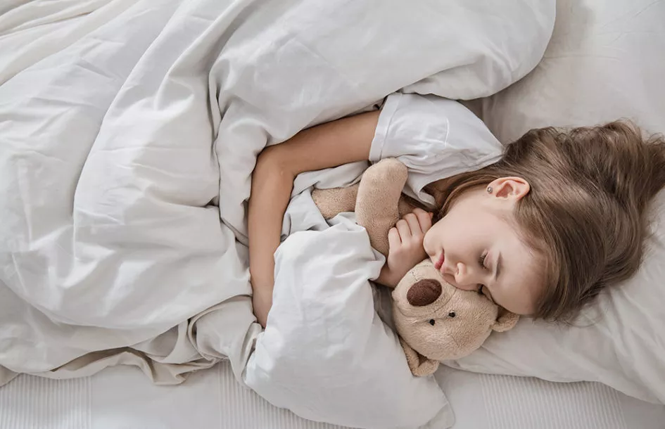 Cute little girl in a white bed sleeping with a soft toy.