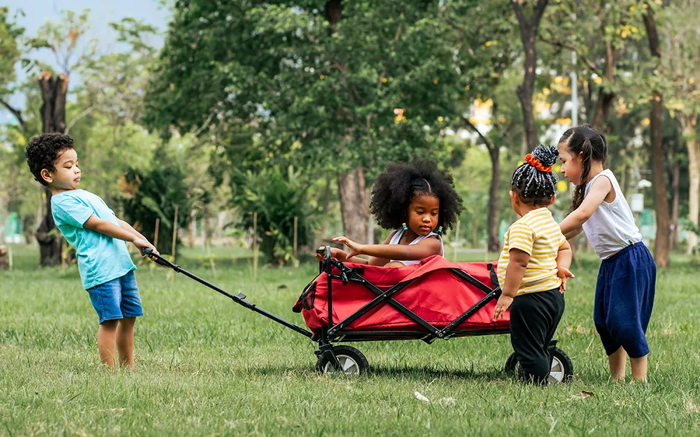 Group of toddlers playing with red wagon.