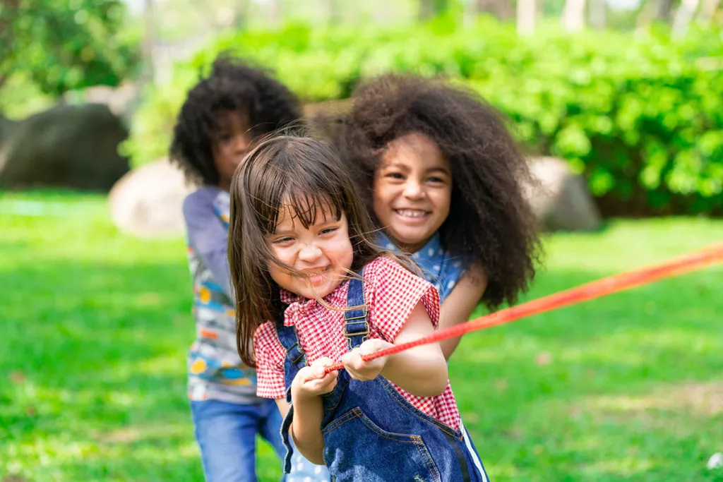Happy children playing tug of war and having fun during summer camp.