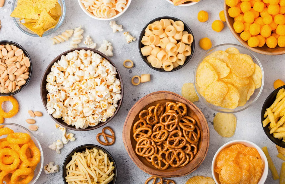Various snack foods on the table, including chips, pretzels, nuts and seeds.