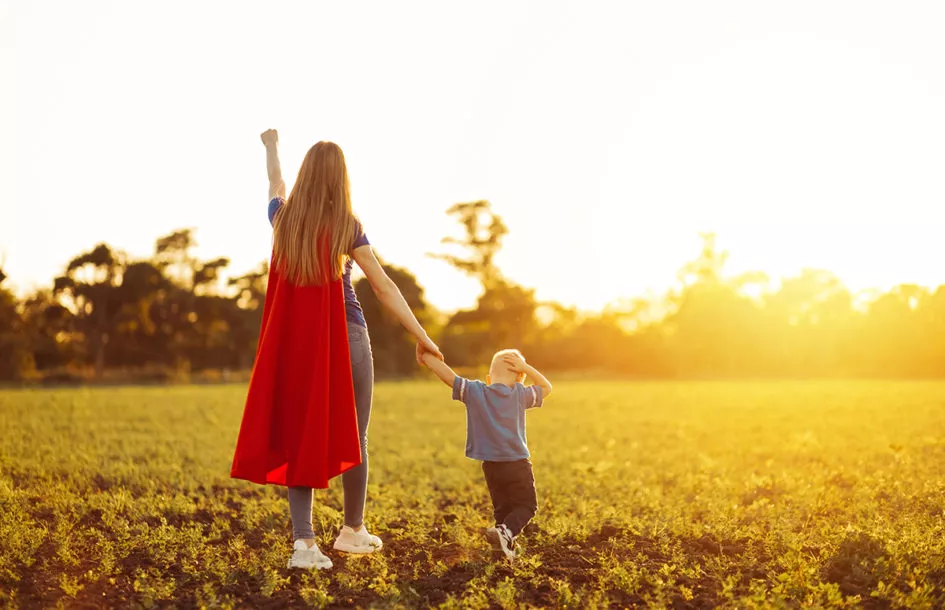 Super mom and her son walk forward holding hands.