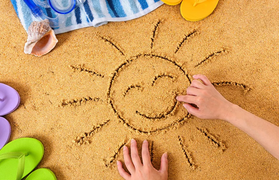 A drawing of smiley sun in sand with towel, seashells and flip flops