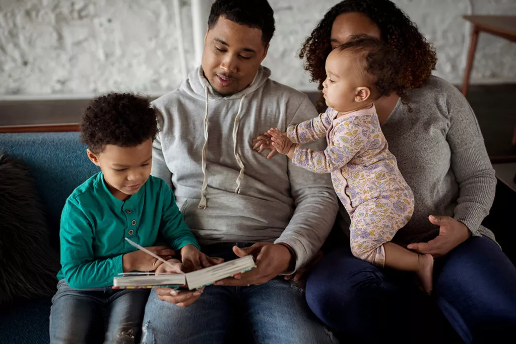 Parents with children relaxing on sofa and reading.