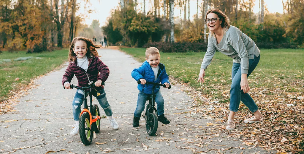 Mother having a walk in the park with her children teaching them to ride the bike