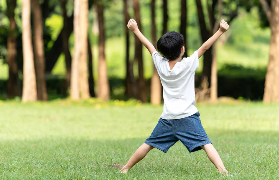 confident little boy raising arms in the park.