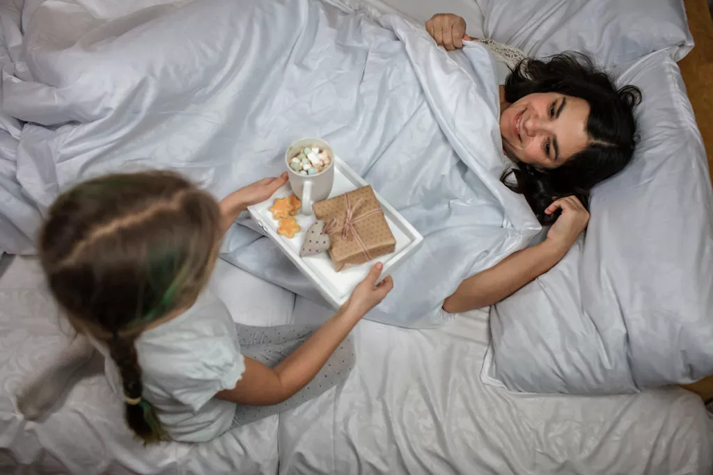Cute little girl giving surprise and gift to her mom in the bed