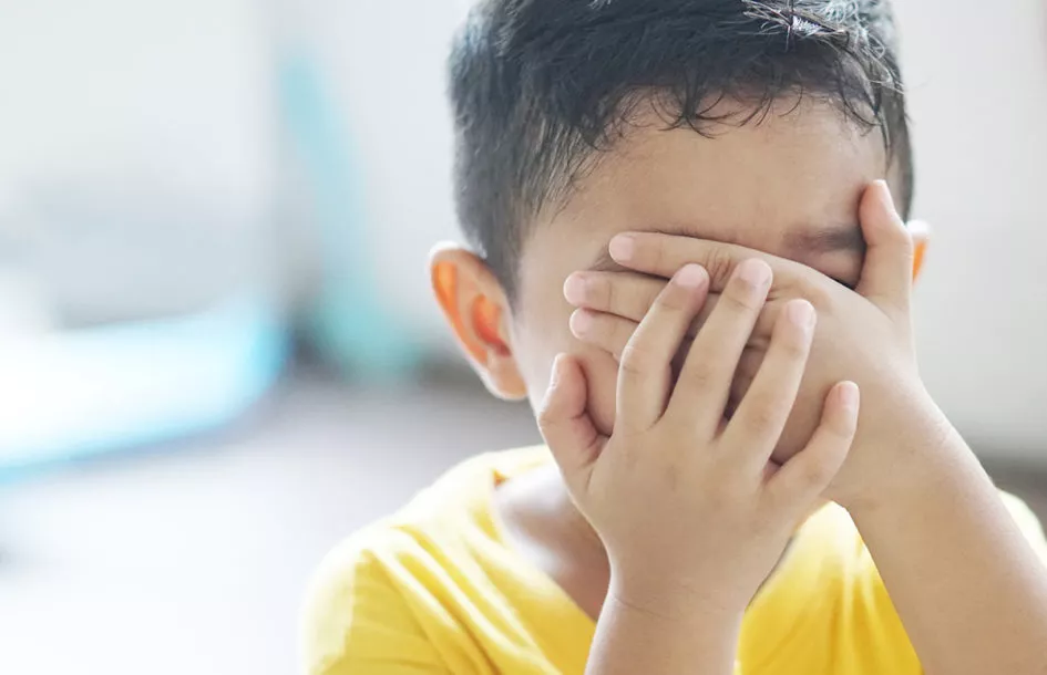 Young boy upset and covering his face with his hand.