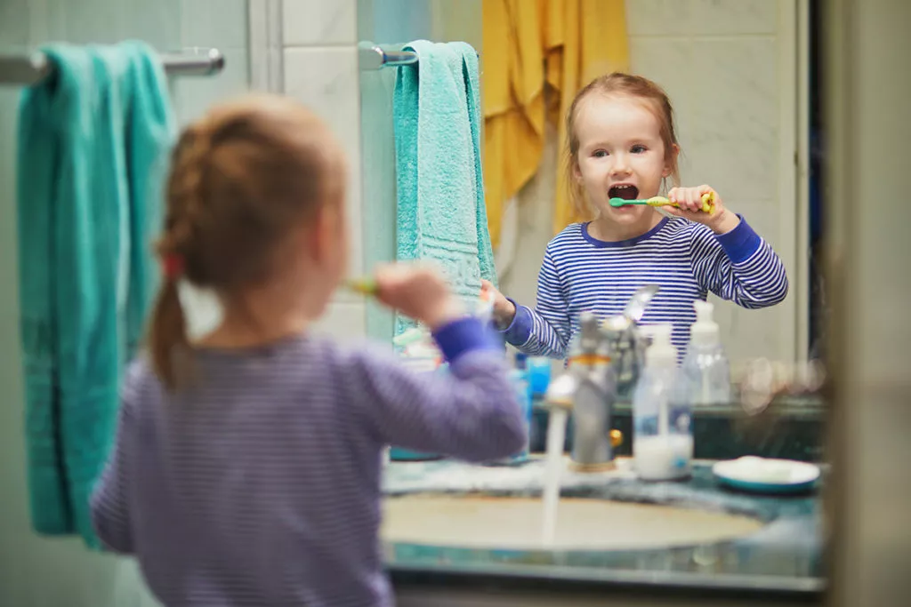 Happy toddler girl in pyjamas brushing her teeth in bathroom