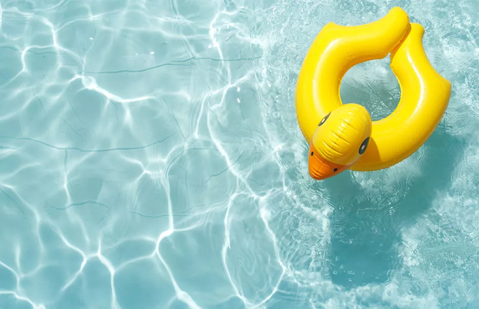 Inflatable float rubber ring in the shape of a yellow duckling in blue pool water.