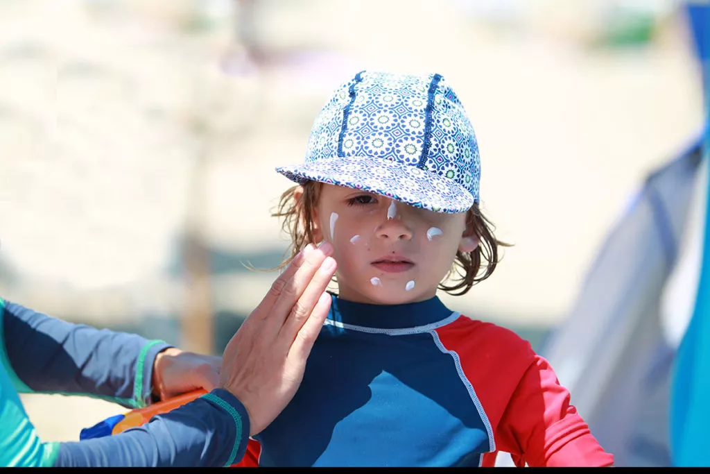 putting sunscreen on a little boy who is wearing a hat and sun shirt