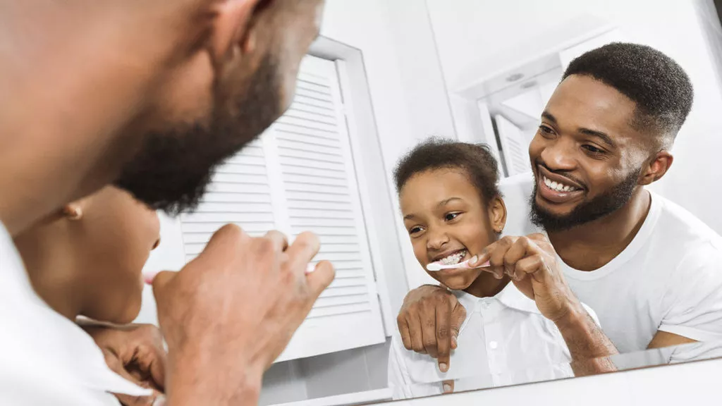 father teaching daughter to brush teeth