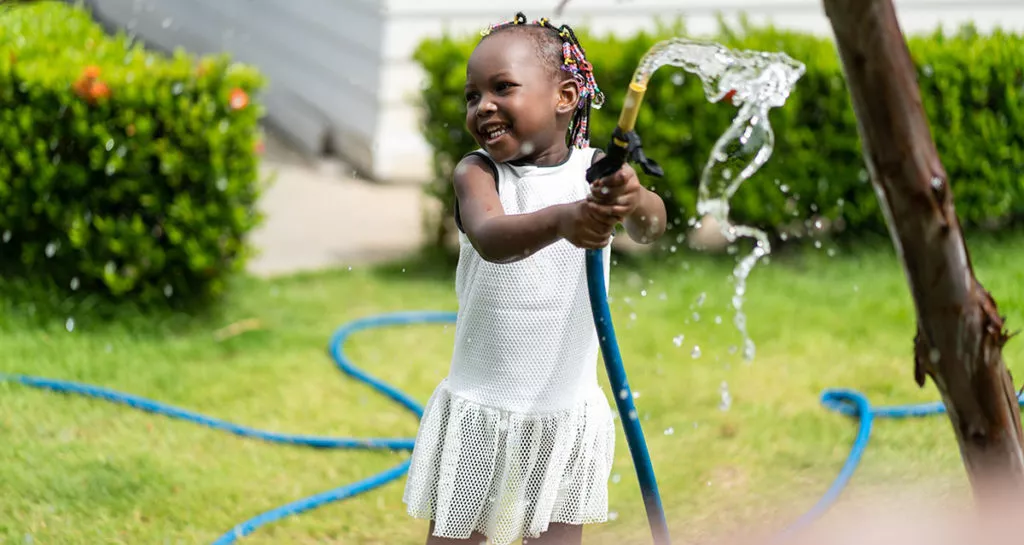 Little girl playing outside with the water hose, enjoying the summer.