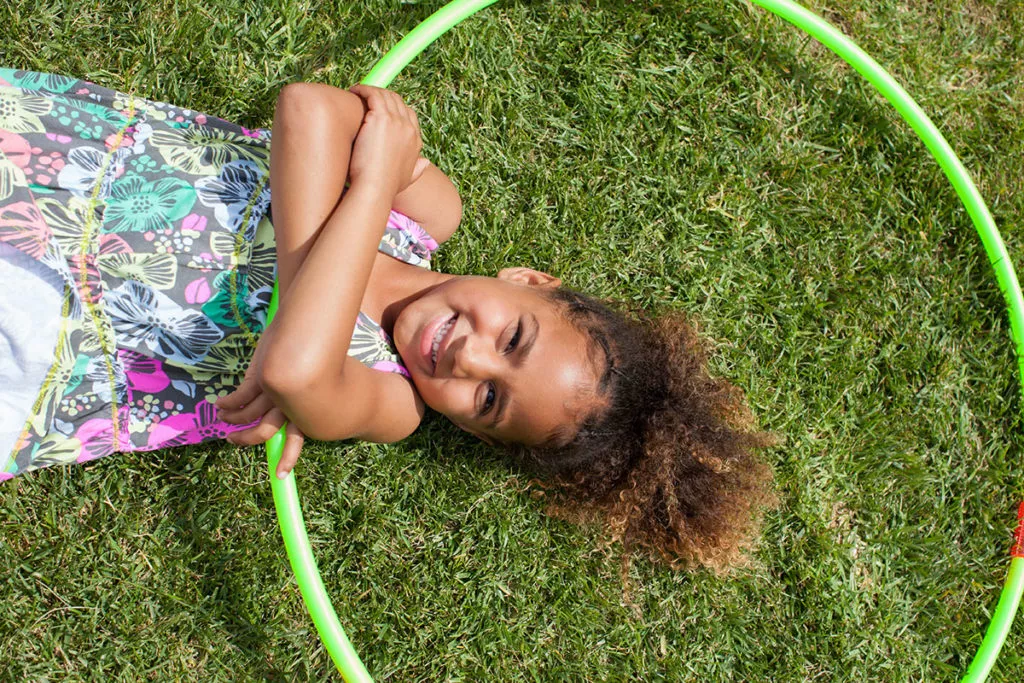 young girl enjoying the summer, laying on grass with her hoola hoop.