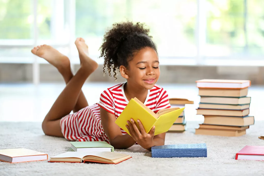 Happy little girl reading a book at home.